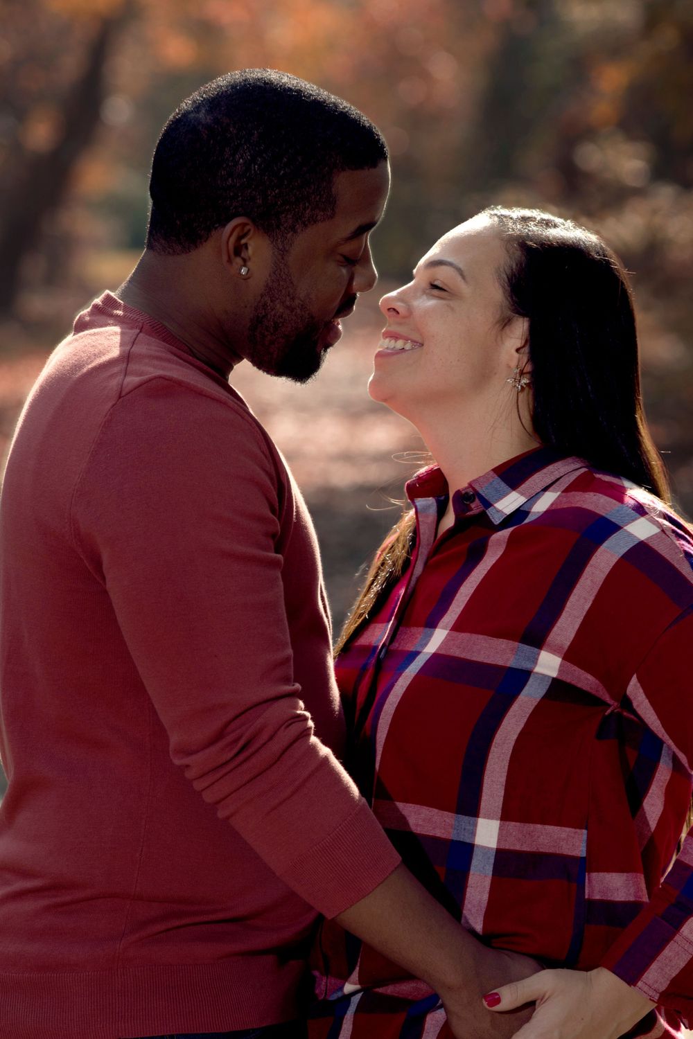A romantic couple wearing red sweaters share an intimate moment outdoors during autumn.