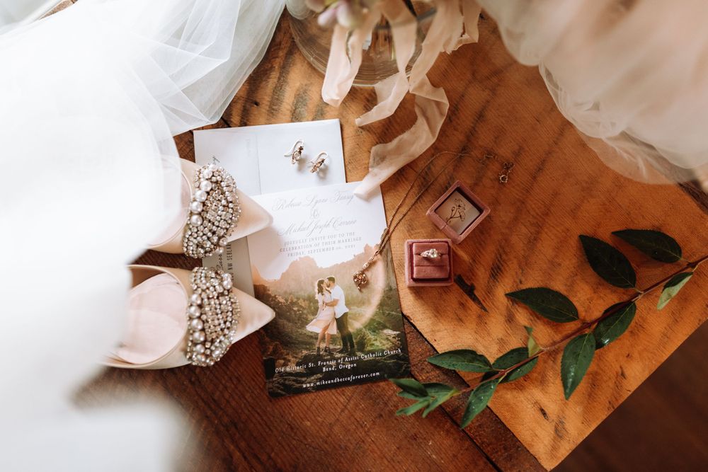 Wedding details including a decorative bow, delicate perfume bottle, and green foliage arranged on brown parchment paper.