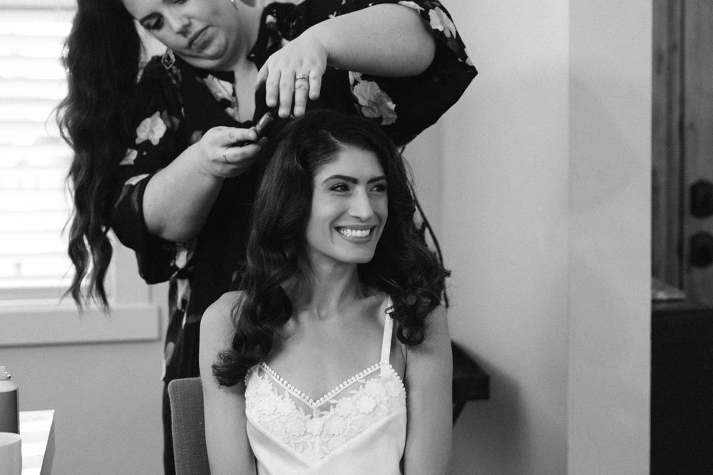 Black and white photo of a hairstylist working on a client's long dark hair in a salon setting.