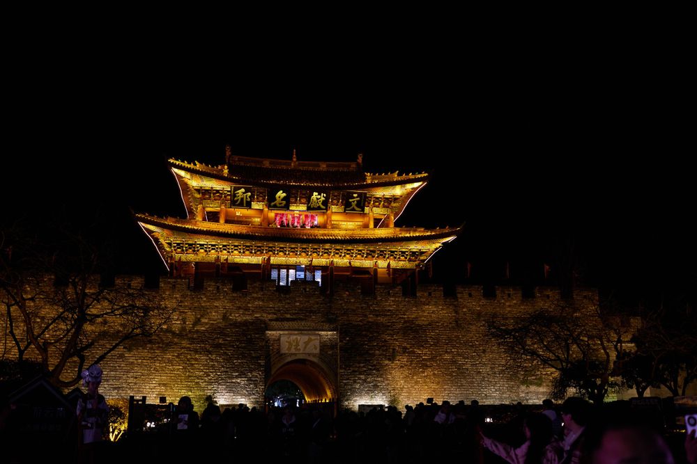 Traditional Chinese pagoda illuminated at night atop ancient stone walls in Lijiang ancient city.