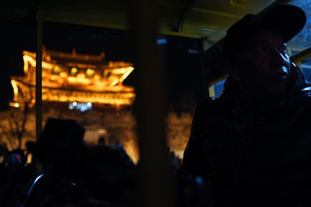 Dark silhouettes of people against a dimly lit background with glowing lights in the distance.