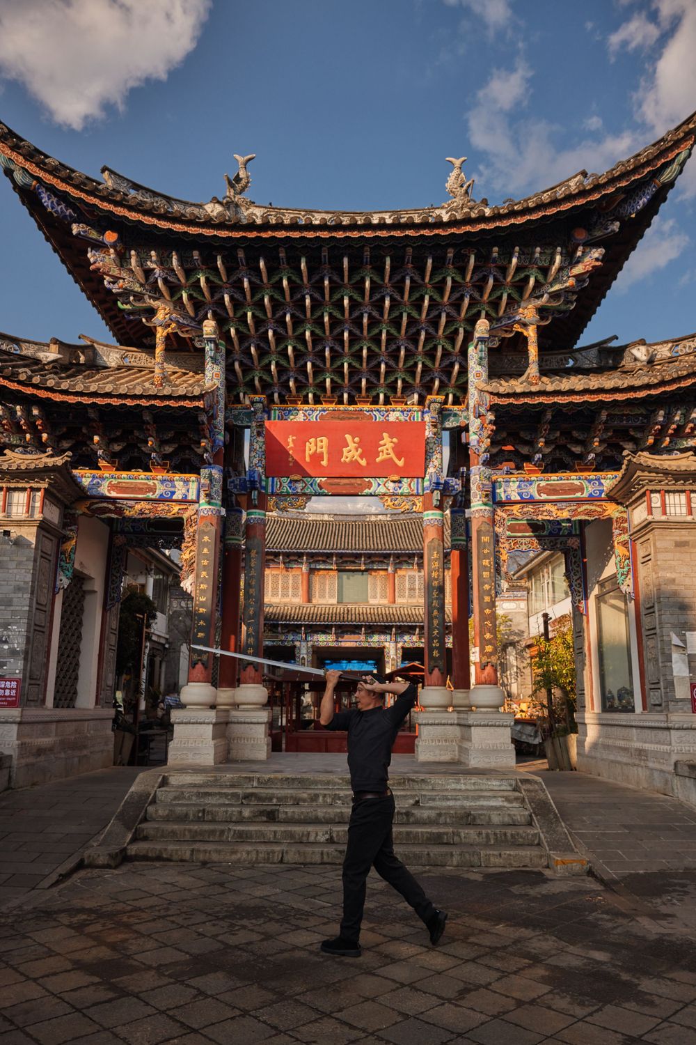 Tourist taking photo at ornate traditional Chinese temple entrance with curved tiled roof and red sign in Dali, China.