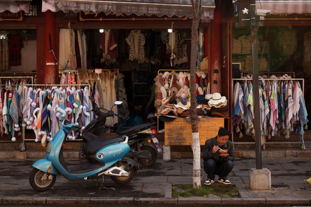 A vintage scooter parked outside a clothing shop with racks of colorful garments on display in Bangkok.
