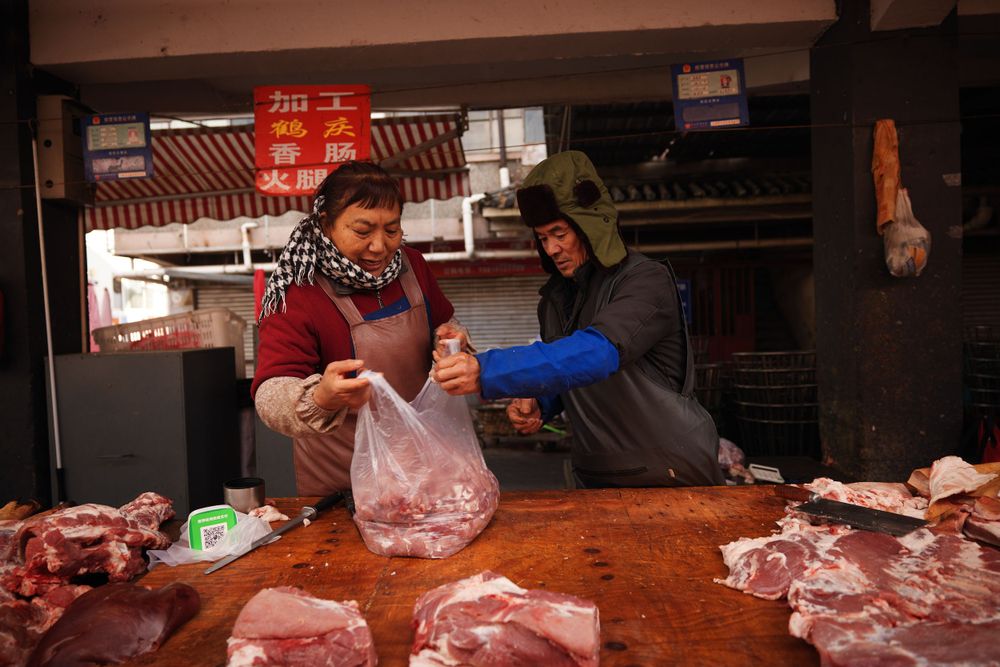 Two vendors discuss business at a butcher counter in a traditional market.