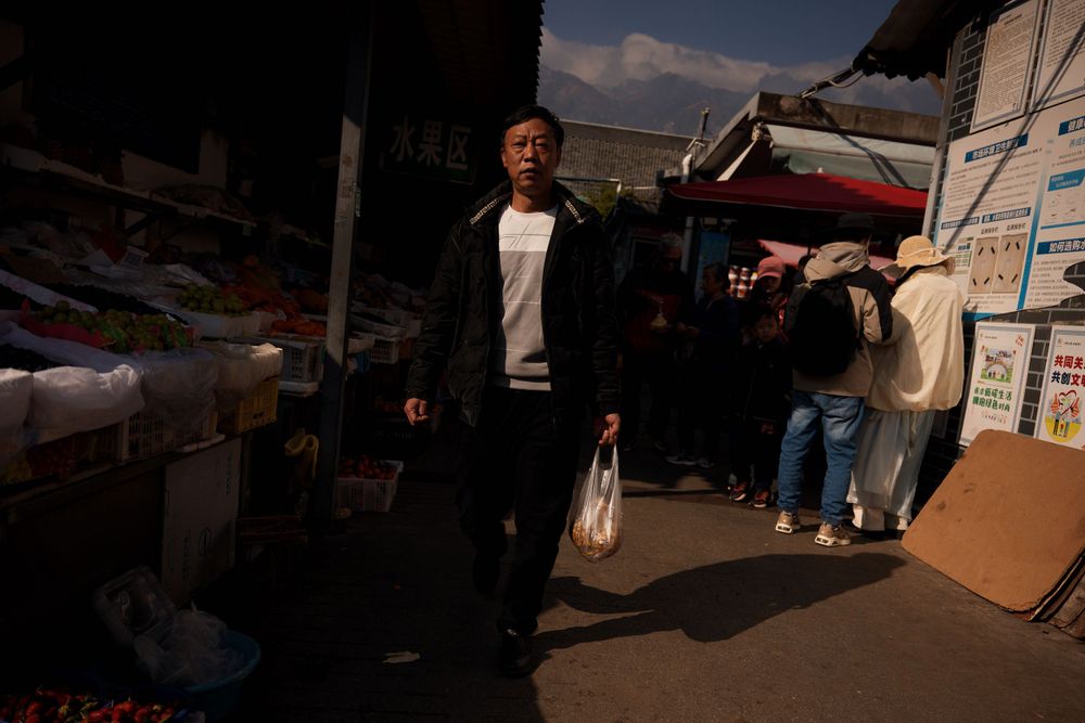 A person walks through a dimly lit outdoor market carrying a shopping bag.