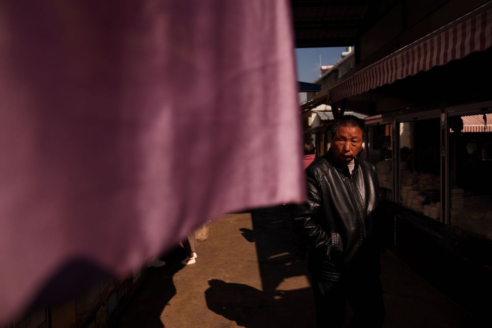 A person stands in shadows against a pink curtain on a sunny day casting dramatic lighting.