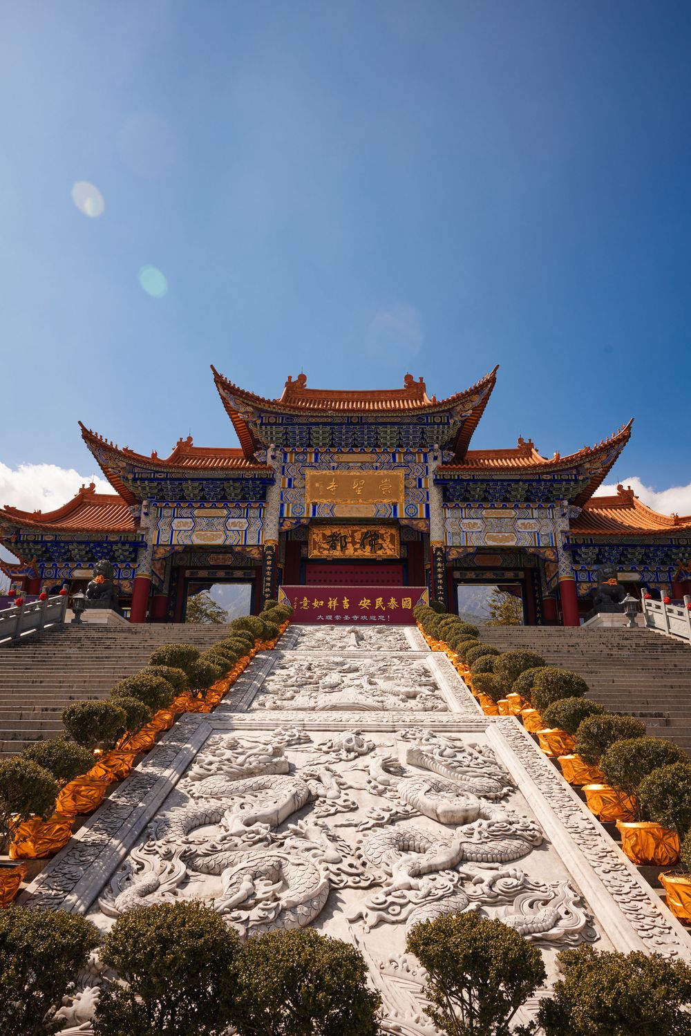 Traditional Chinese temple with ornate rooftops and dragon-carved steps leading to entrance under bright blue sky.