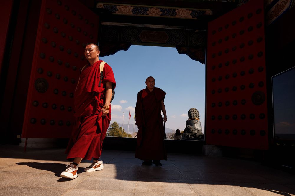 Buddhist monks in traditional red robes walk through an ornate temple doorway at sunset.