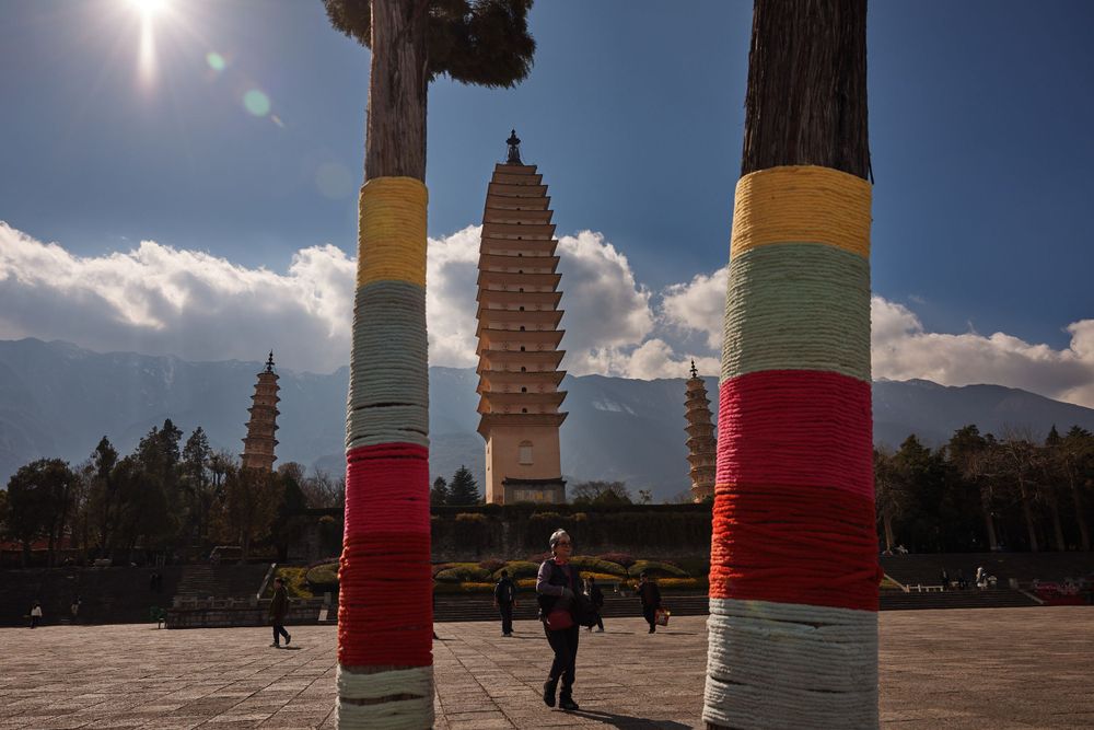 Ancient pagodas at Three Pagodas Temple in Dali, China with colorfully striped pillars in the foreground against blue sky.