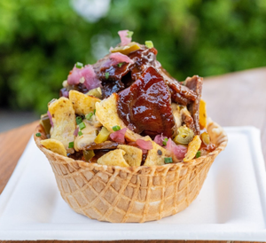 Gourmet loaded nachos served in a waffle cone bowl with barbecue sauce and toppings.
