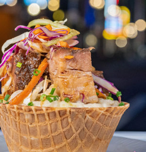 Gourmet pulled meat sandwich topped with colorful slaw served in a crispy waffle cone bowl.
