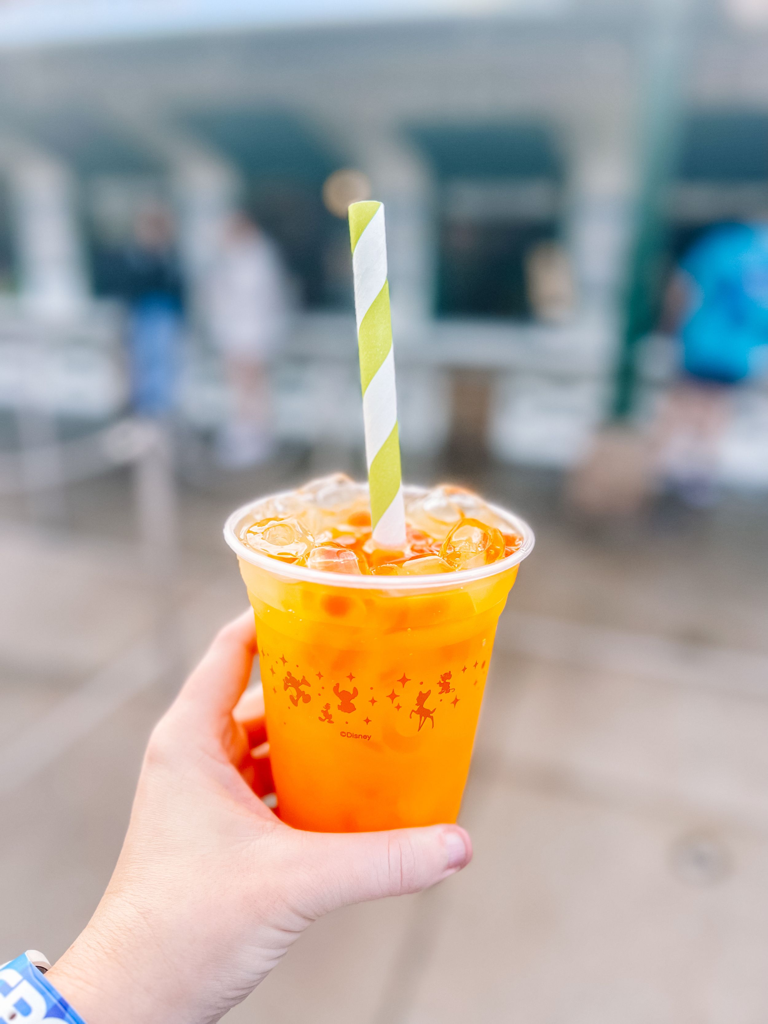 Orange frozen drink with green striped straw in clear plastic cup against blurred background.