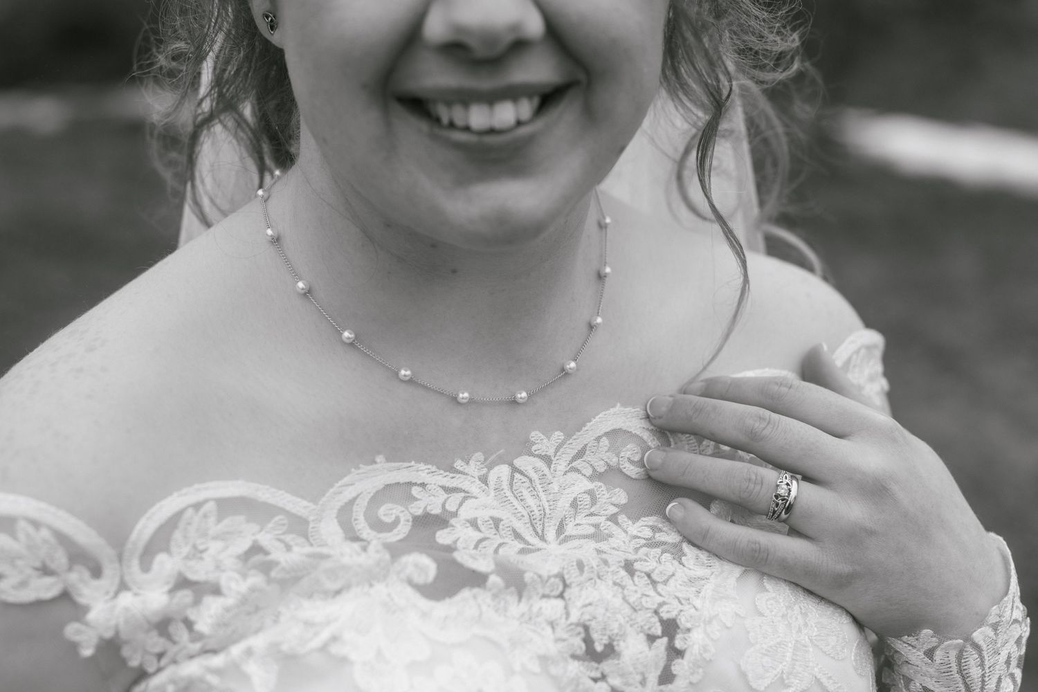 Close up black and white detail of bridal lace dress and delicate pearl necklace.