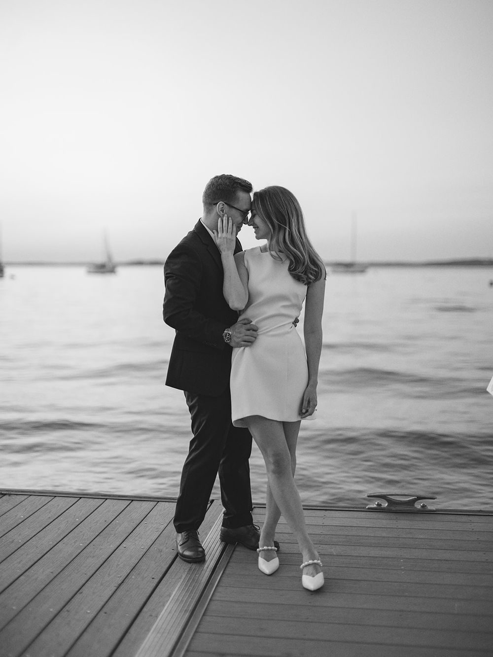 Romantic couple embracing on wooden dock at sunset with boats in background.