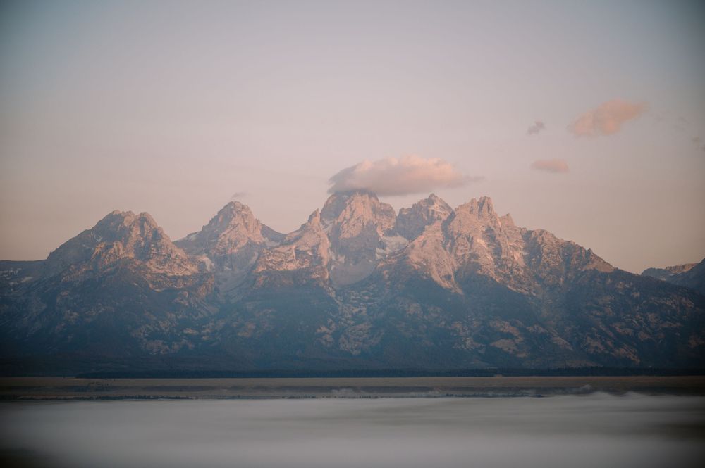 Snow-capped Teton mountain range reflected in calm lake waters at sunset.