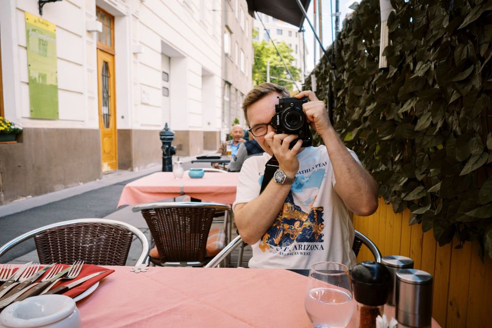 Photographer taking photos while seated at outdoor cafe table.