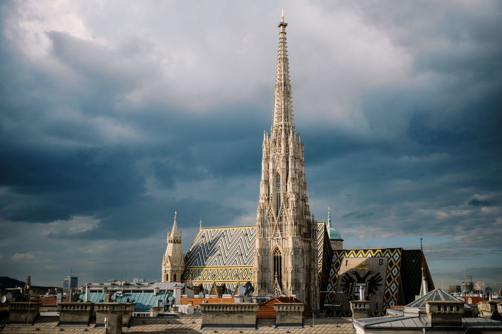 Gothic cathedral spire rises against dramatic stormy sky in Vienna.