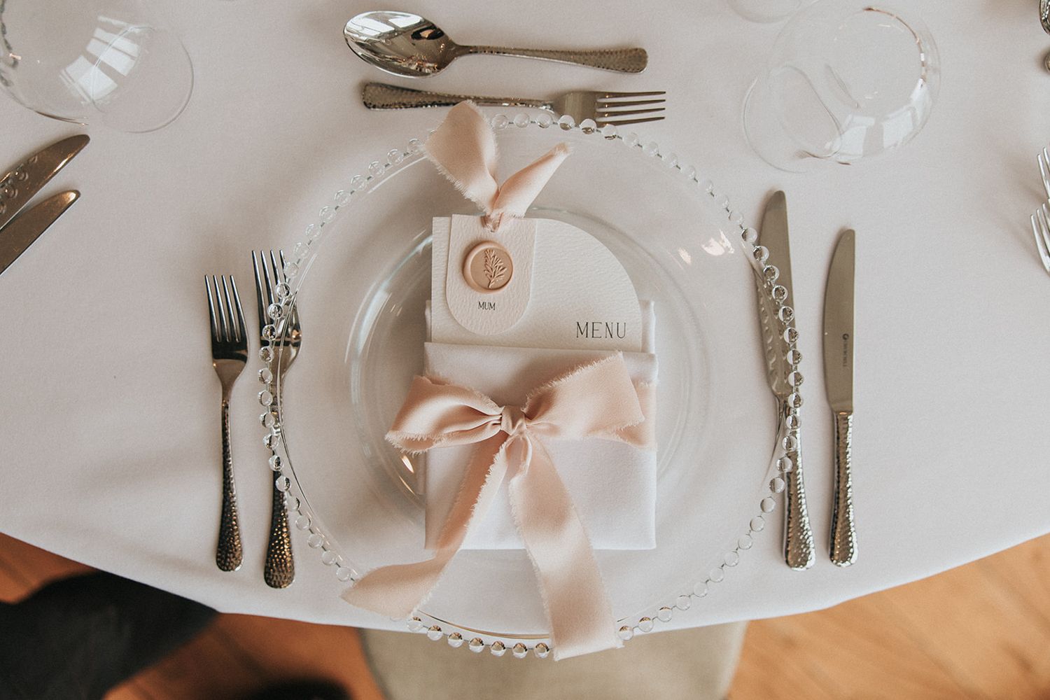 Elegant place setting with white plate and peach ribbon favor bag on white tablecloth at wedding reception.