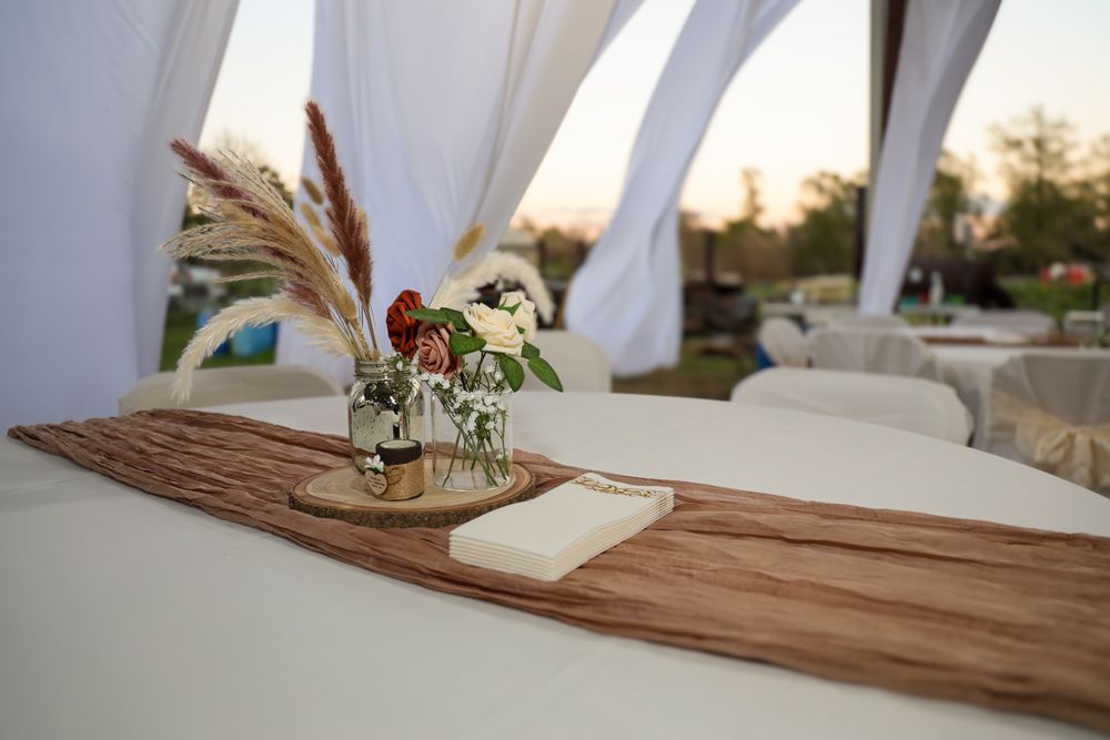 A rustic wooden table surface with white linens and elegant place settings in a bright outdoor dining space.