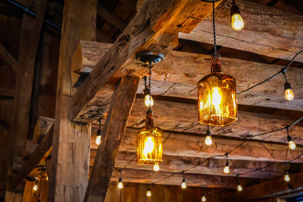 Rustic barn ceiling with vintage mason jar pendant lights and Edison bulbs hanging from wooden beams.