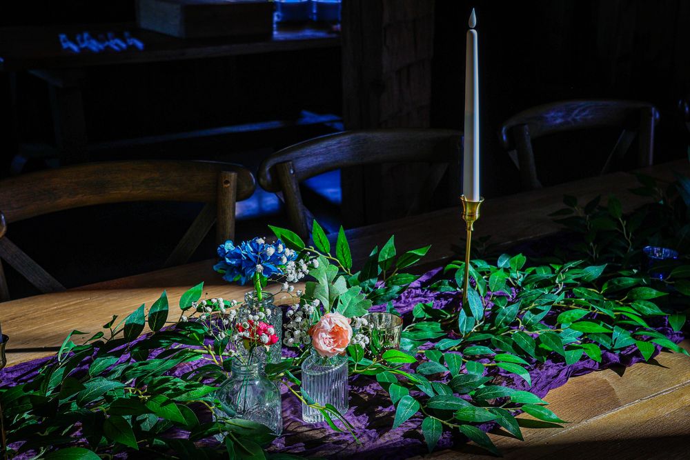 Elegant wedding table centerpiece with candle, greenery, and colorful flowers in a rustic venue.