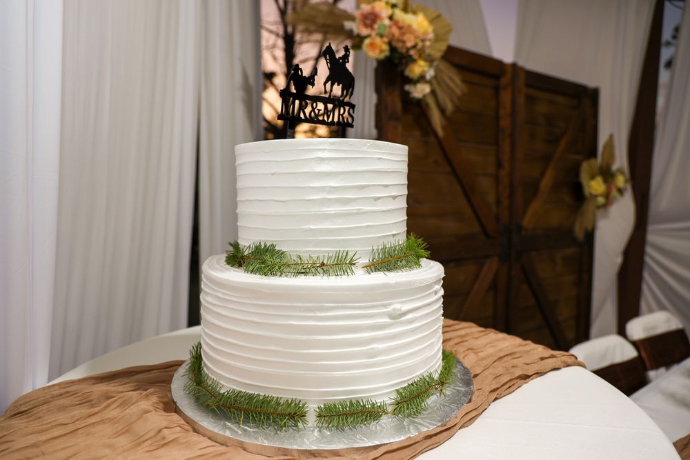 White tiered wedding cake with textured frosting and green moss accents displayed on rustic wooden table.