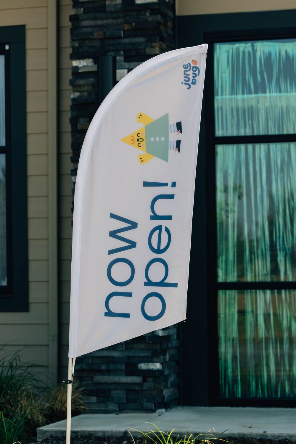 White feather flag with Junebug logo announcing now open outside a new childrens play space.