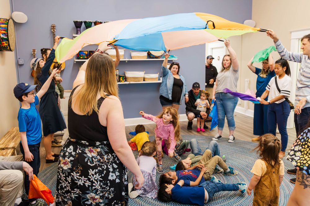 Children and adults playing with a colorful parachute during a Family Rhythms music and movement class.