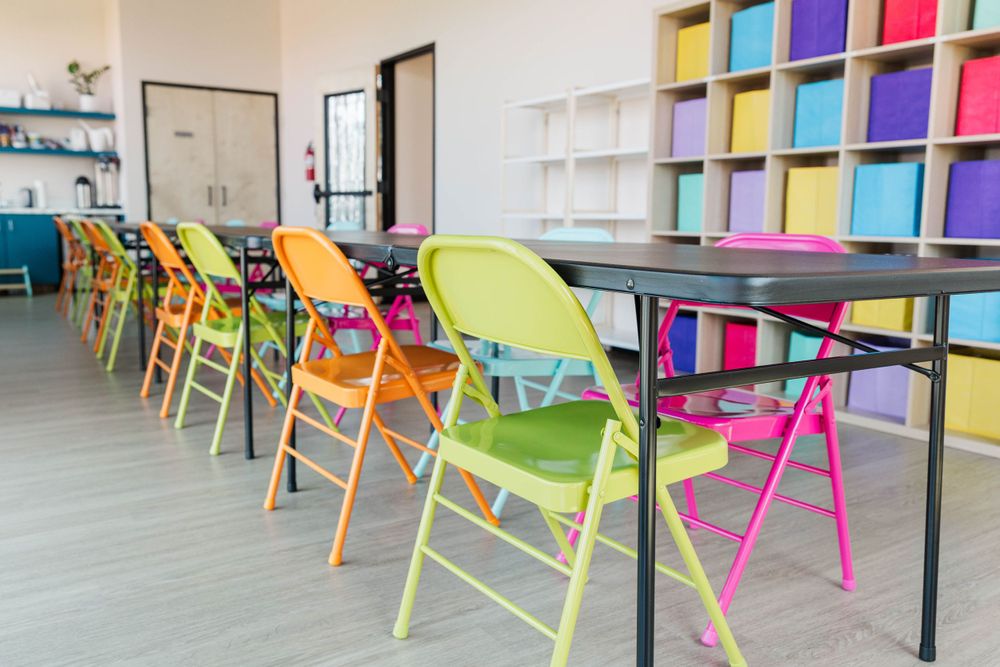 Rows of vibrant multicolored folding chairs lined up along black tables in a cheerful, well-lit activity room.