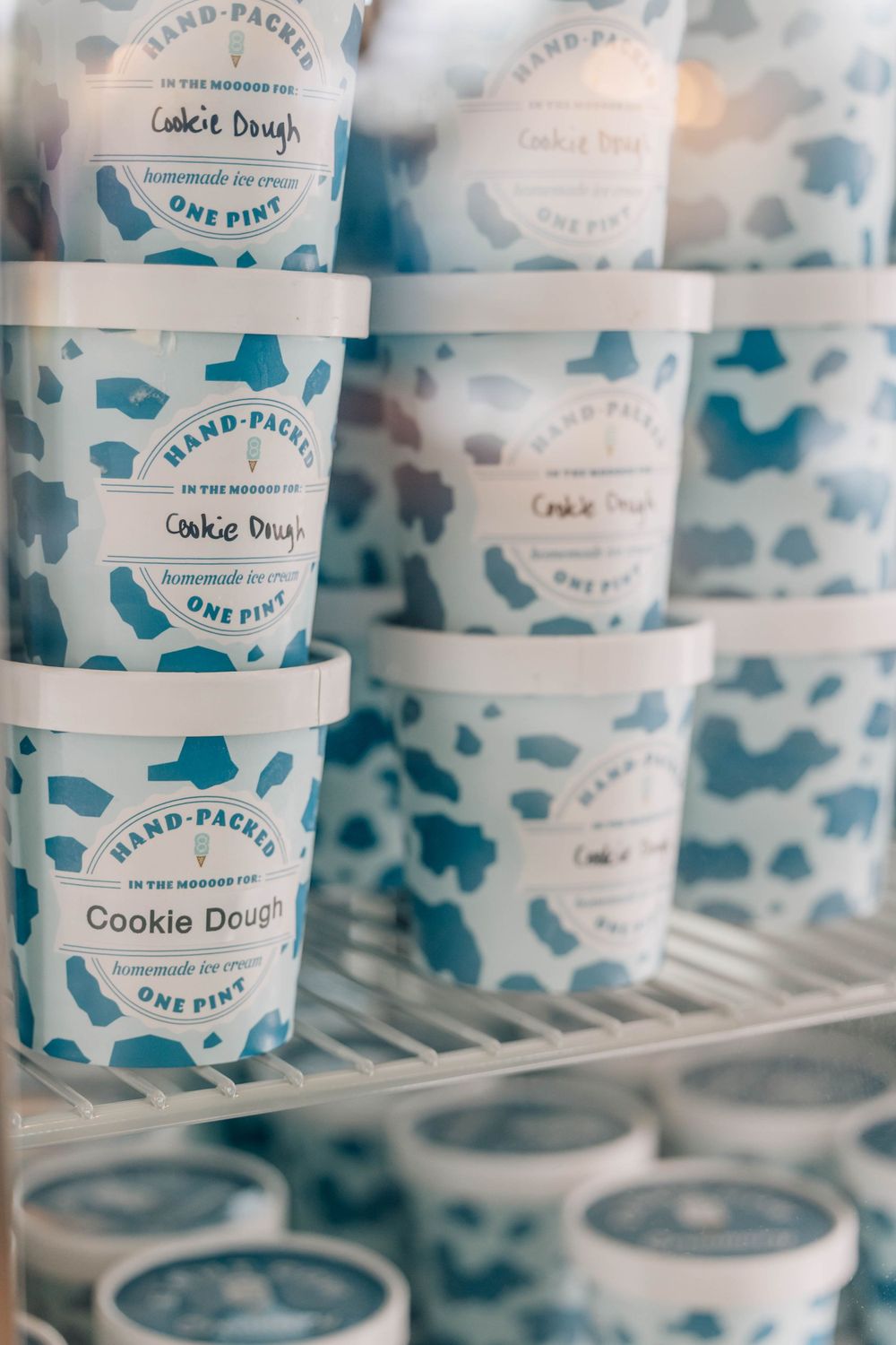 Shelves stocked with hand-packed one pint Cookie Dough homemade ice cream containers with blue cow print design.