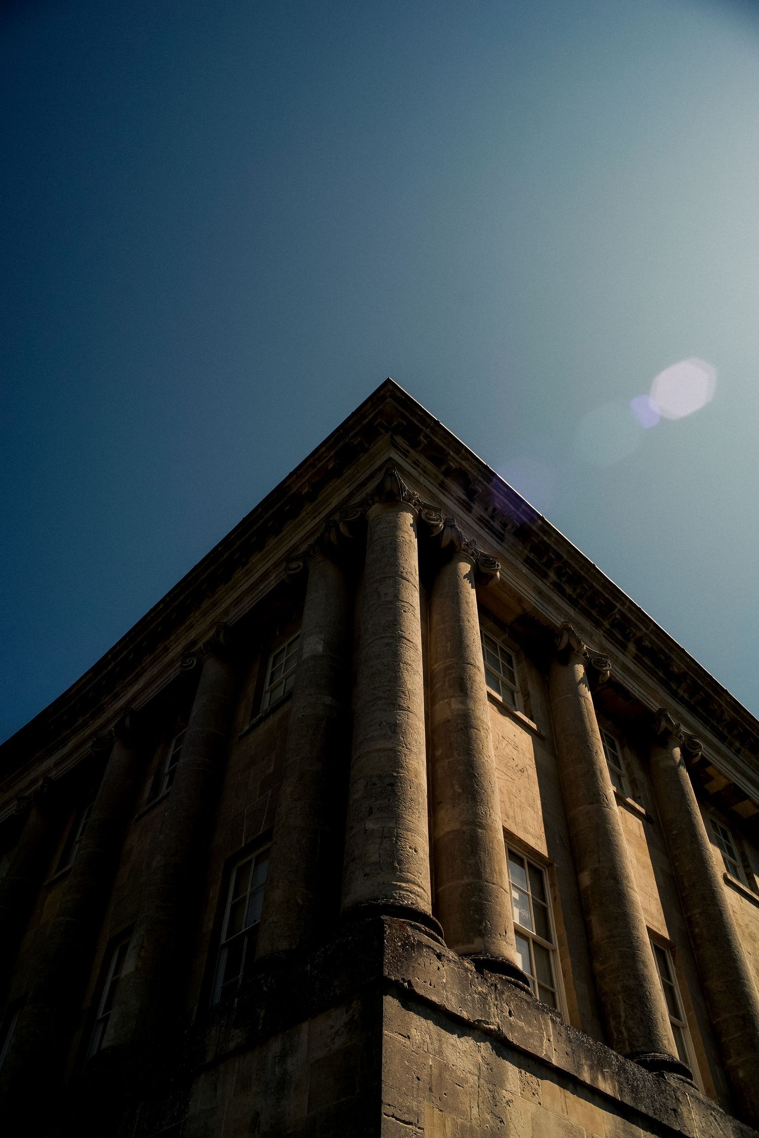 Low angle view of neoclassical columns and architecture against a deep blue sky with lens flare.