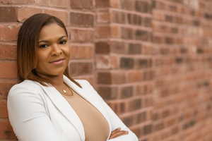 Professional portrait photograph with white blazer against red brick wall background.