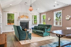 Modern coastal living room with white shiplap walls, emerald velvet sofa and chairs, and decorative hanging pendant light.