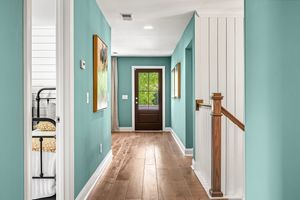 Bright entrance hallway with turquoise walls, hardwood floors, and natural light streaming through a glass-paned door.