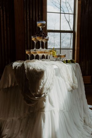 A champagne tower display on an elegant white tablecloth by a window.
