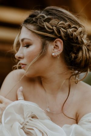A romantic wedding hairstyle with intricate braids and pearl earrings shown in warm sepia tones.