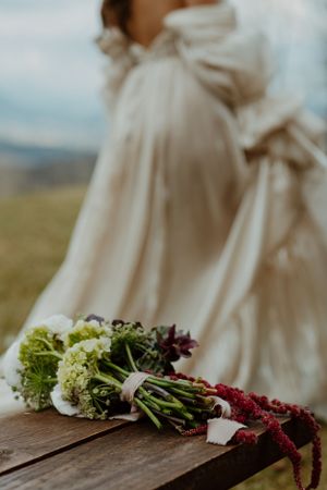 Wedding dress detail with floral arrangements on rustic wooden surface.