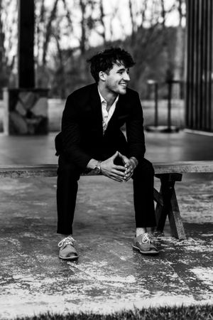 Black and white portrait of a person in formal attire crouching playfully.
