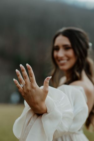 Close-up of an engagement ring on a hand with a wedding dress in the background.