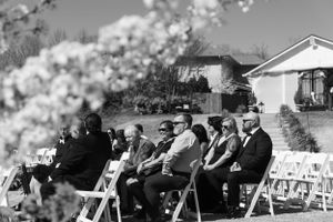 Black and white photo of wedding guests seated in rows of white chairs during outdoor ceremony.