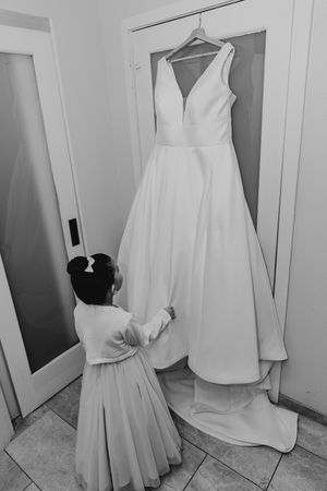 Black and white image of flower girl admiring hanging wedding dress in doorway.