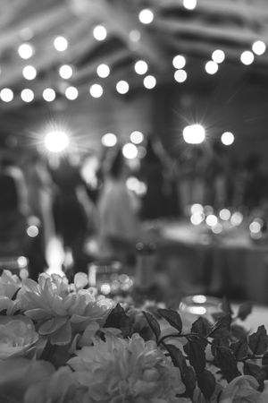 Beautiful black and white reception photo with bokeh lights and floral centerpieces in the foreground.