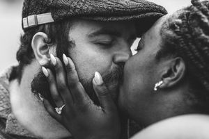 An intimate black and white close-up of a tender romantic kiss between two lovers, with one wearing a flat cap.