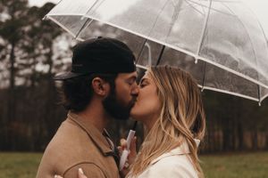 Couple sharing a romantic kiss under a clear umbrella with forest scenery behind them.