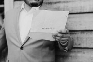 Black and white close-up of person in suit holding letter or note.