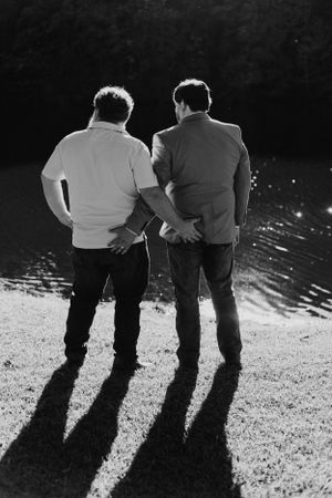 Black and white silhouette of two people standing by water at sunset.