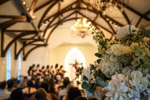 Wedding reception venue with exposed wooden beams and elegant white floral arrangements adorning the rustic interior.