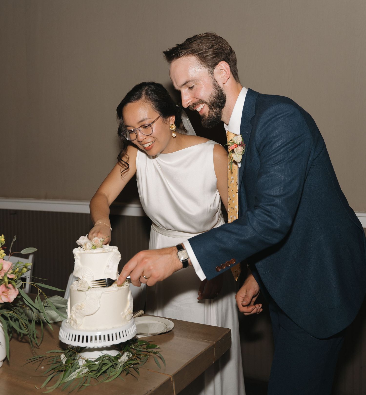 Newlyweds cut their white wedding cake together at the reception.