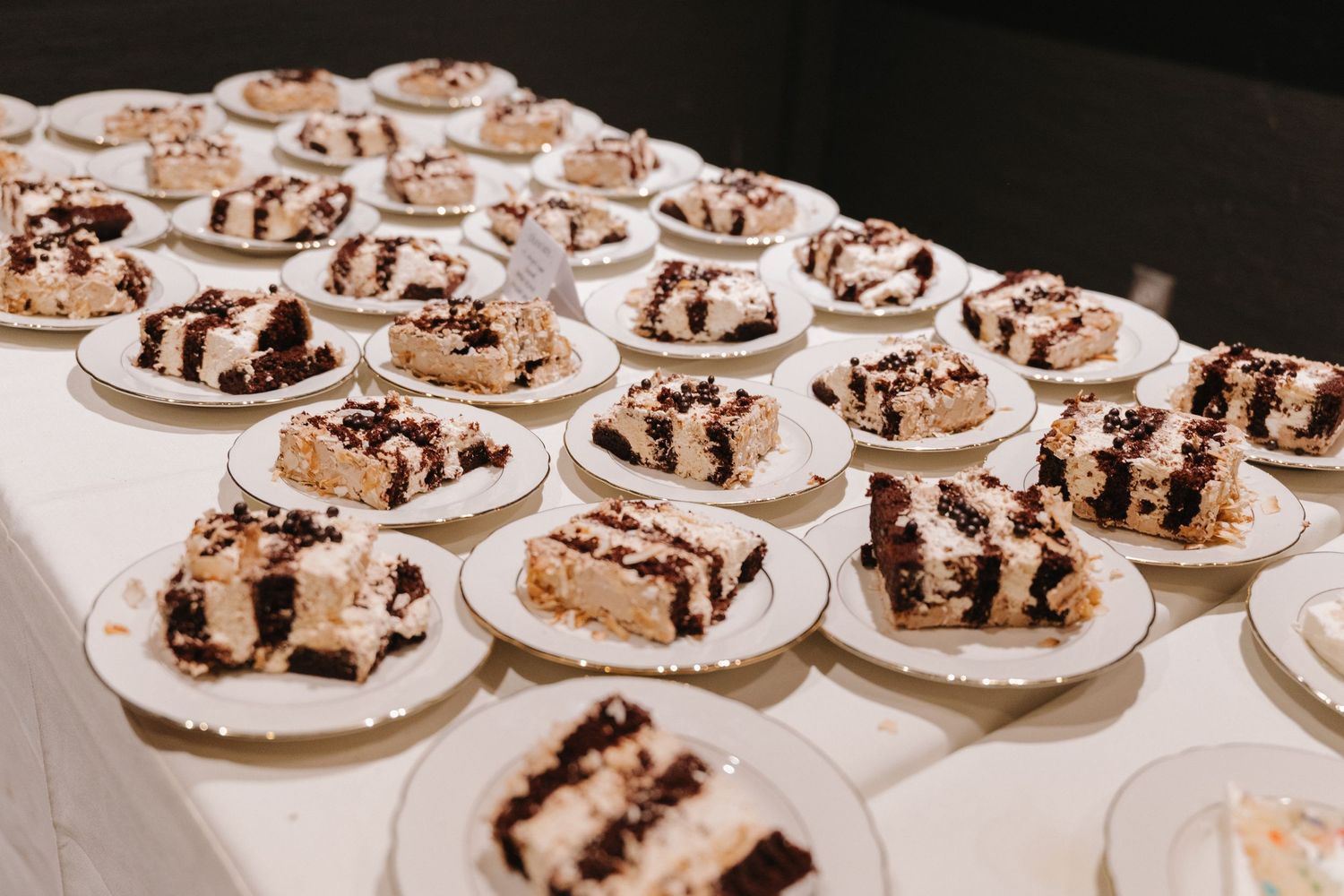 Multiple plates of chocolate drizzled dessert slices arranged on a white tablecloth.