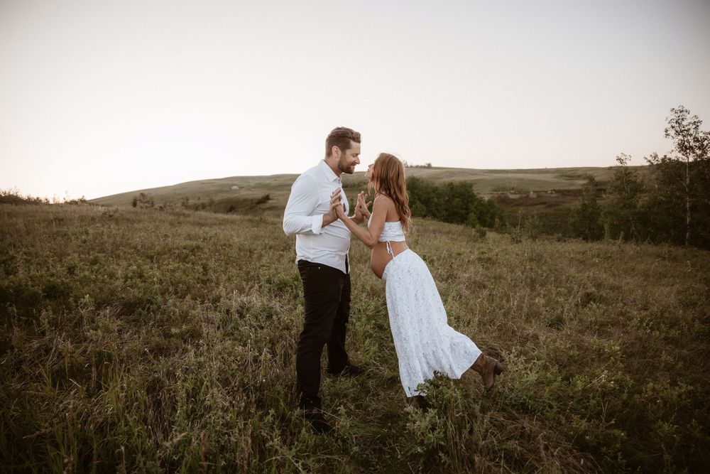 A romantic sunset moment captured in a rustic field with rolling hills in the background.